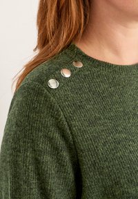 Groene gebreide trui met een textuurpatroon, voorzien van drie metalen knopen op de linker schouder.