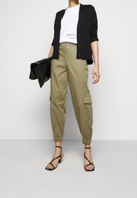 Sort cardigan, hvid t-shirt med print, olivengrøn cargo-bukser og sorte sandaler med stropper. Glatte teksturer, afslappet pasform og elastiske manchetter.