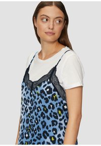 Cami-jurk in blauw met een luipaardprint, voorzien van zwarte kantafwerking. Draagt over een wit t-shirt met opgerolde mouwen, wat een casual gelaagd uiterlijk laat zien.