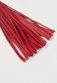 Czerwone skórzane frędzle o teksturowanej powierzchni rozłożone na białym tle.