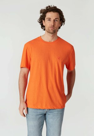 Orange bomulds t-shirt med korte ærmer, rund halsudskæring og et lille logo-patch på brystet. Strukturstof, afslappet pasform, kombineret med lyse jeans.