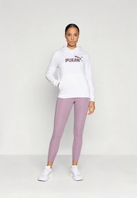 Witte hoodie met "PUMA"-logo in bordeauxrood, gecombineerd met lichtpaarse leggings en witte sportschoenen. Strak, modern ontwerp.