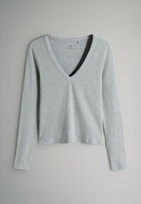 Gaiši pelēks garām piedurknēm krekls ar V veida kaklu, mīksta tekstūra un brīvs piegriezums. Nav redzami nekādi raksti vai papildu rotājumi.