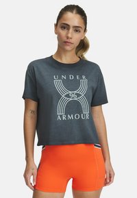 Camiseta corta de color gris oscuro con un diseño gráfico blanco que presenta "UNDER ARMOUR" y "96". Combinada con pantalones cortos de color naranja brillante y detalles deportivos.