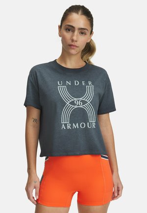 Donkergrijze cropped t-shirt met een witte grafische afbeelding met "UNDER ARMOUR" en "96". Gecombineerd met feloranje shorts en sportieve details.