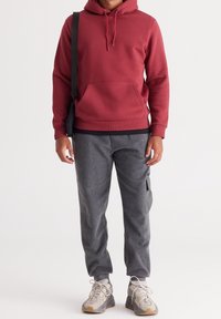 Röd hoodie med framficka, tillsammans med grå tapered byxor med sidofickdetalj och lätta sneakers.