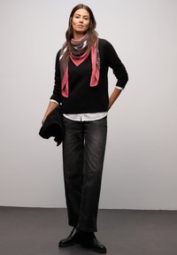 Sort sweater lag-på-lag over en hvid skjorte, kombineret med løse sorte jeans. Et pink og mønstret tørklæde tilføjer farve, og sorte ankelstøvler fuldender looket.