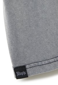 Tessuto grigio con texture liscia, caratterizzato da un'etichetta nera con la scritta "Utopia" in un font stilizzato sul bordo. Design semplice e casual.