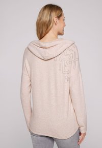 Felpa con cappuccio rosa chiaro realizzata in morbido tessuto, caratterizzata da una vestibilità rilassata, orlo arrotondato e ricamo argentato sul retro.