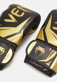Black and gold boxing gloves made of leather, featuring a textured surface and bold graphic design with angular patterns and embossed accents.