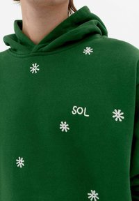 Green hoodie with a soft texture, featuring white embroidered flowers and the word "SOL" in white, located on the front area.