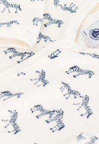 Body bianco per bebè con stampe di tigri a righe blu, caratterizzato da una texture morbida, scollo rotondo e chiusura a scatto sul davanti.