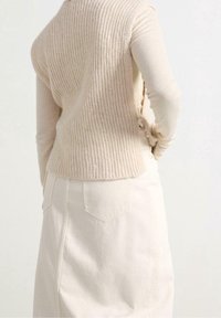 Beige geribbelde gebreide mouwloze trui gelaagd over een lange mouwen top, gecombineerd met een off-white denim rok met een achterzak.