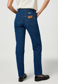 Jeans in denim blu con un motivo in rilievo, tasche posteriori e una patch in pelle con il marchio. Design aderente con gamba dritta e leggero stretch.