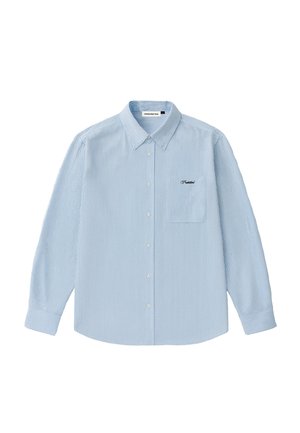 Hombre con camisa de botones a rayas blancas y azul claro con bolsillo en el pecho y pantalones marrones, de pie frente a un fondo liso.