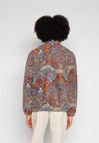 Giacca patterned con una vestibilità rilassata, caratterizzata da motivi paisley in tonalità di marrone, blu e arancione, con polsini elastici e colletto alto.