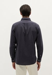 Donker marineblauwe overhemd met lange mouwen en een button-down kraag, rugplooien en knopen aan de manchetten. Gemaakt van een zachte stof met een gladde textuur.