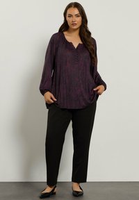 Blusa viola a maniche lunghe con un motivo testurizzato e scollatura a V. Abbinata a pantaloni neri e décolletées nere. Presenta un dettaglio con bottone al collo.