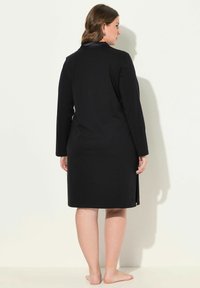 Vestido negro de manga larga con corte recto, que presenta un cuello de cuero y aberturas laterales, fabricado en una tela suave y lisa.