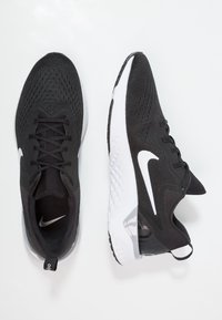 Černé sportovní boty s pružnou síťovinou, obsahující bílé logo swoosh, texturované detaily a gumovou podrážku. Na patě je průhledný akcent.