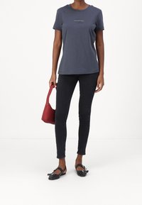 Tmavě modré bavlněné tričko s krátkými rukávy a logem, v kombinaci s černými úzkými džíny, červenou kabelkou a černými balerínkami s přezkami.