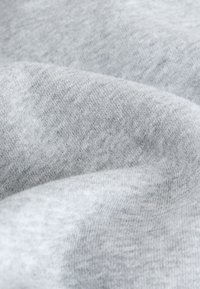 Gros plan d’un tissu doux gris clair avec une texture fine en maille et des plis délicats.