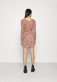 Vestido ajustado de manga larga con un estampado de leopardo rojo y negro. Cuenta con un escote en la espalda y detalles de fruncido en la cintura, combinado con botas negras.