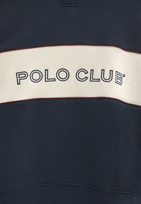 Mörkblå sweatshirt med krämfärgad rand som har "POLO CLUB" i mörkblå bokstäver, ribbad nederkant och kontrasterande vinröd pipingdetaljer.
