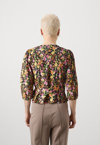Blommig blus i svart med livfulla mönster i rosa, orange och grönt. Puffärmar och en peplummidja ger volym och struktur.