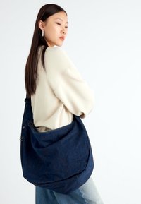 Sac à épaule en bleu marine, en tissu durable et au style décontracté, avec une finition texturée, une bandoulière réglable et une poche avant avec des accents en métal.