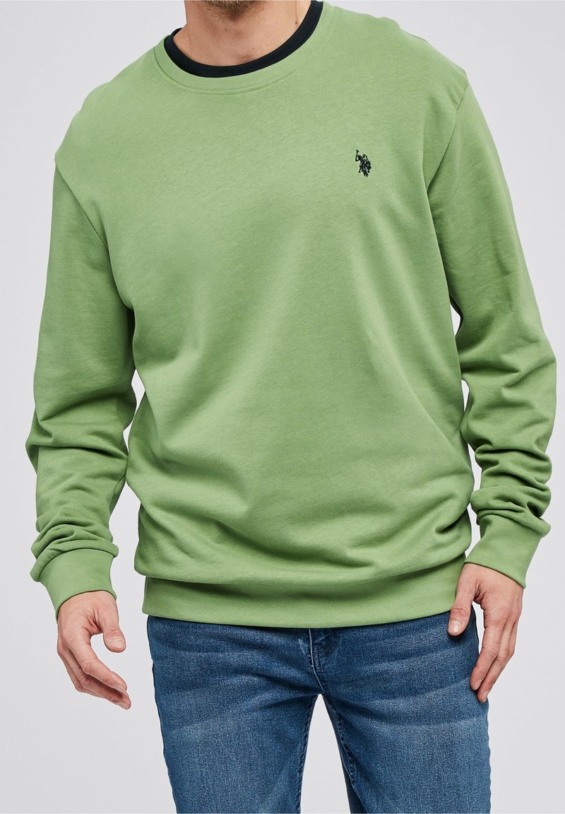 Vihreä huppari, jossa on pyöreä kaulus ja pitkät hihat, valmistettu pehmeästä kankaasta, jossa on hienovarainen logo korostus rinnassa.