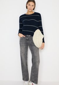 Navy striped knit sweater with white lines, paired with light gray wide-leg jeans and a cream shoulder bag. White and red sneakers complete the look.