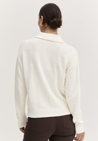 Cremefarvet, chunky strikket sweater med ombukket krave, ribbede manchetter og kant. Bæres med mørkebrun bukser. Struktureret stof, afslappet pasform.
