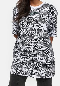 Bílá oversized tričko s černými abstraktními liniovými vzory a smajlíky. Krátké rukávy, kulatý výstřih a hladký bavlněný materiál.