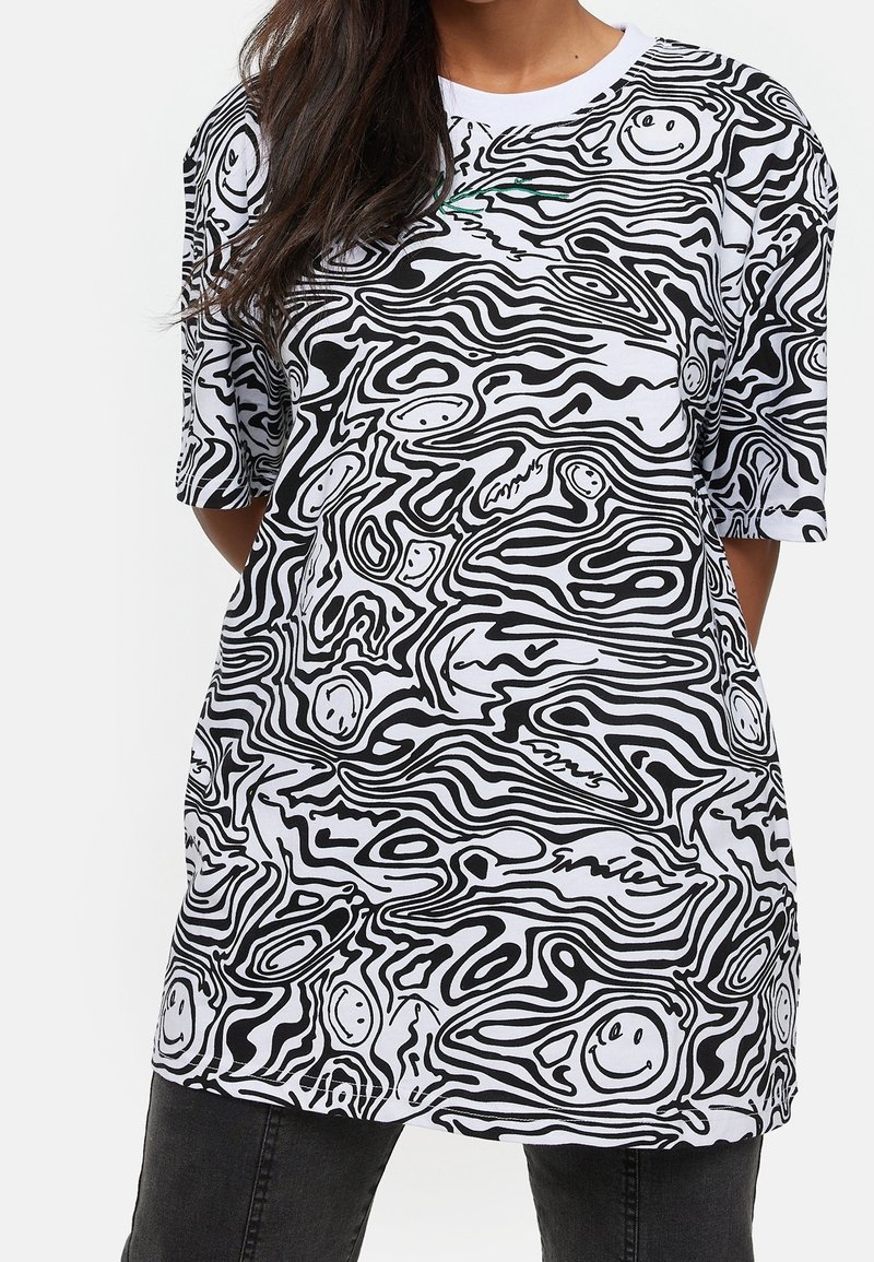 Bílá oversized tričko s černými abstraktními liniovými vzory a smajlíky. Krátké rukávy, kulatý výstřih a hladký bavlněný materiál.