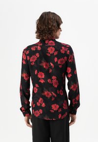 Sort langærmet skjorte med rødt blomstermønster, med krave og knapmanchetter. Glat tekstur, buet kant bagpå.