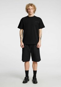 Svart bomulls-t-skjorte med korte ermer og rund hals, kombinert med svarte shorts som går til knærne. Enkel design uten synlige mønstre.