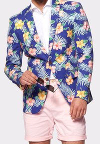 Kwiatowa marynarka na niebieskim tle z różowymi i żółtymi kwiatami, noszona na białej koszuli i zestawiona z różowymi szortami.