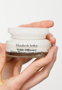 White round cream jar with a frosted lid, labeled "Elizabeth Arden Visible Difference Refining Moisture Cream Complex." Glass base visible.