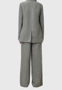 Šedý lněný oblek s upraveným blejzrem s jedním rozventem a kalhotami s širokými nohavicemi pro volný střih. Matný povrch a knoflíkové detaily.