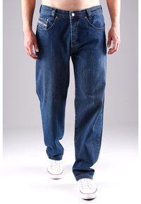 Dunkelblaue Denim-Jeans mit lockerer Passform, ausgestattet mit kupferfarbenen Beschlägen, vorderen Taschen und einem Knopfverschluss, kombiniert mit weißen Sneakern.