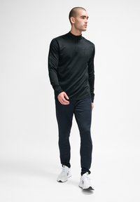Zwarte lange mouwen sportshirt met een kwart rits en logo, gecombineerd met marineblauwe tapered broek en witte sportschoenen. Glad oppervlak.