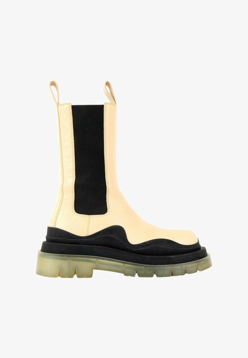 Botte mi-mollet en cuir beige et noir avec une semelle épaisse translucide à crampons et des panneaux élastiques latéraux, avec deux languettes de traction en haut.