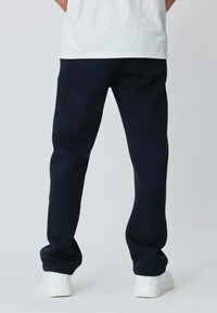 Pantalons de survêtement bleu marine à coupe décontractée, avec une taille élastique et des ourlets resserrés. Portés avec des baskets blanches. La texture semble douce et lisse.