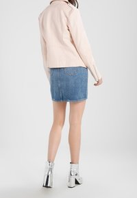 Rosa Lederjacke, Jeansrock und metallische Knöchelstiefel. Das Outfit hat ein figurbetontes Design und glänzende Texturen mit einem sauberen, modernen Look.