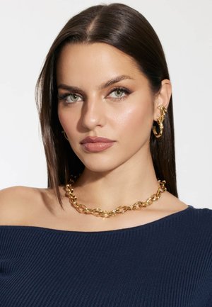 Gold chain necklace with linked oval links, worn over a navy ribbed top. Large hoop earrings accentuate the look. Smooth, shiny finish.