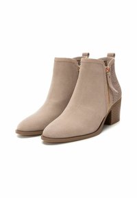 Botas de tobillo beige de ante, con punta afilada, un pequeño tacón, cremallera lateral y acentos perforados en la parte trasera.