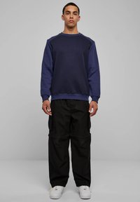 Tumesinine puuvillane dressipluus raglaanvarrukatega, kombineeritud lahtiste mustade cargo-pükstega. Modell kannab valgeid tenniseid. Lihtne ja mugav lõige.