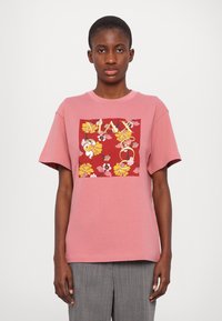 Rosa bomulls t-skjorte med et firkantet blomsterdesign i rød, gul og hvit med "MAX" i fete bokstaver. Korte ermer og avslappet passform.