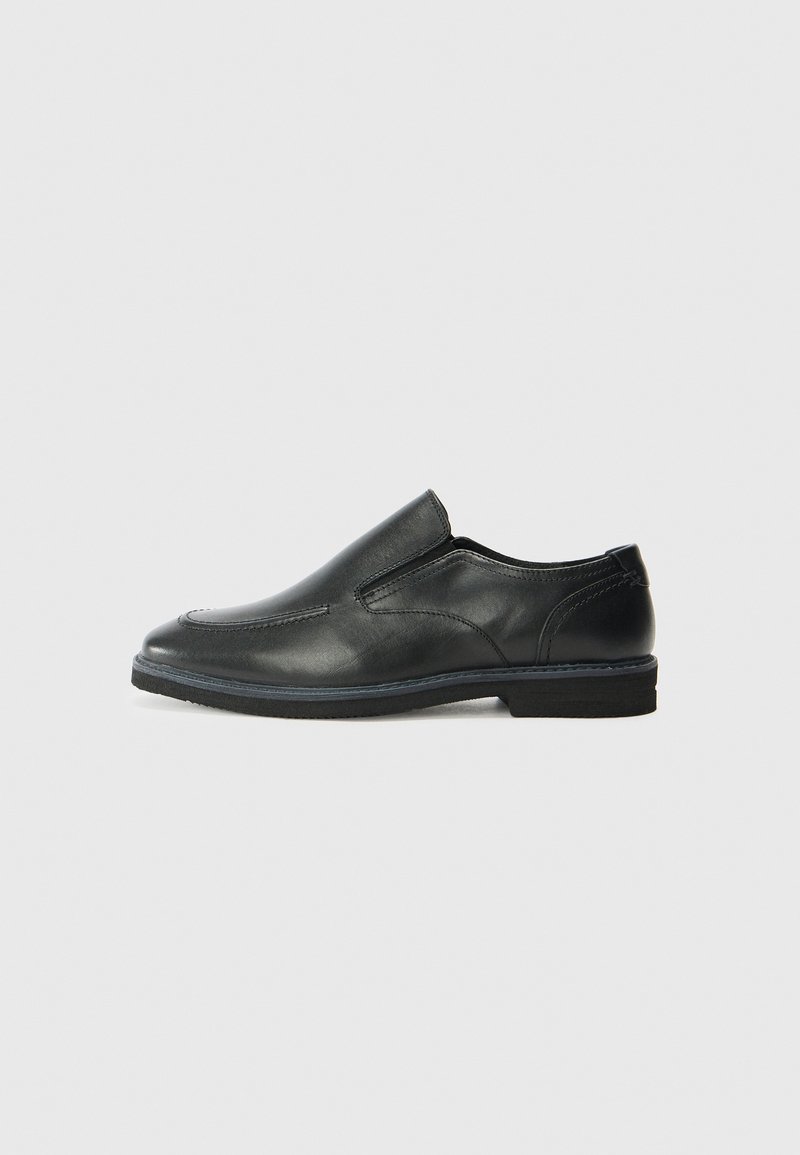Black leather slip-on shoe with a smooth upper, stitched accents, rounded toe, and a low rubber heel. Sole features minimal tread.